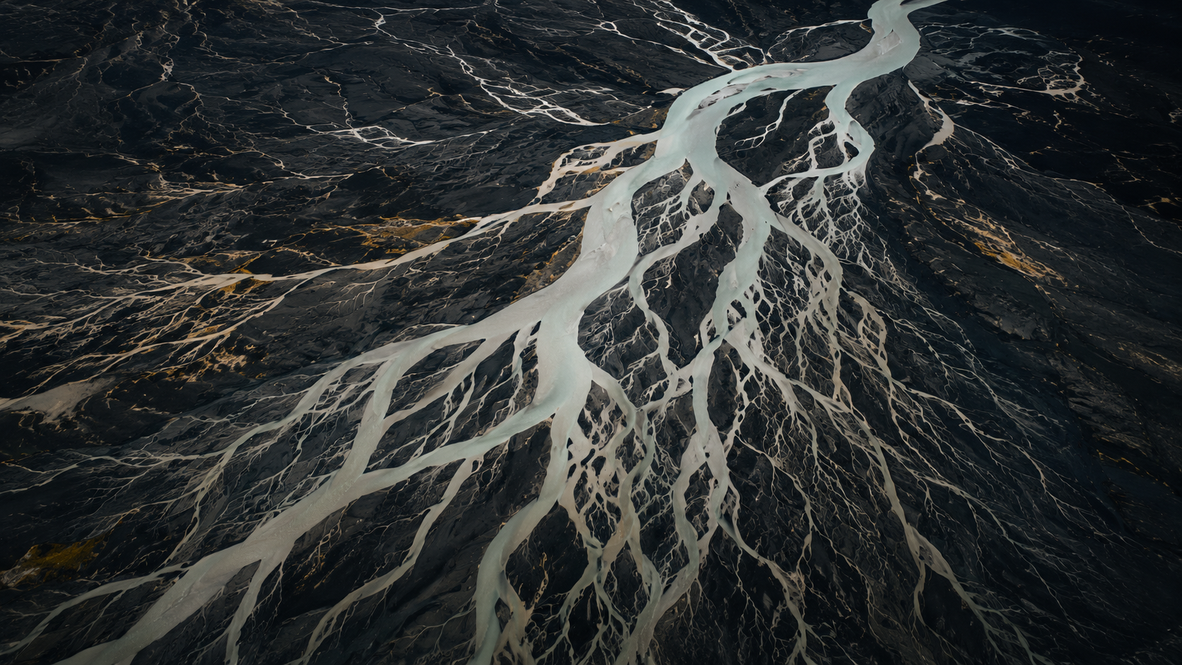 Aerial view of a braided glacial river system spreading across dark terrain